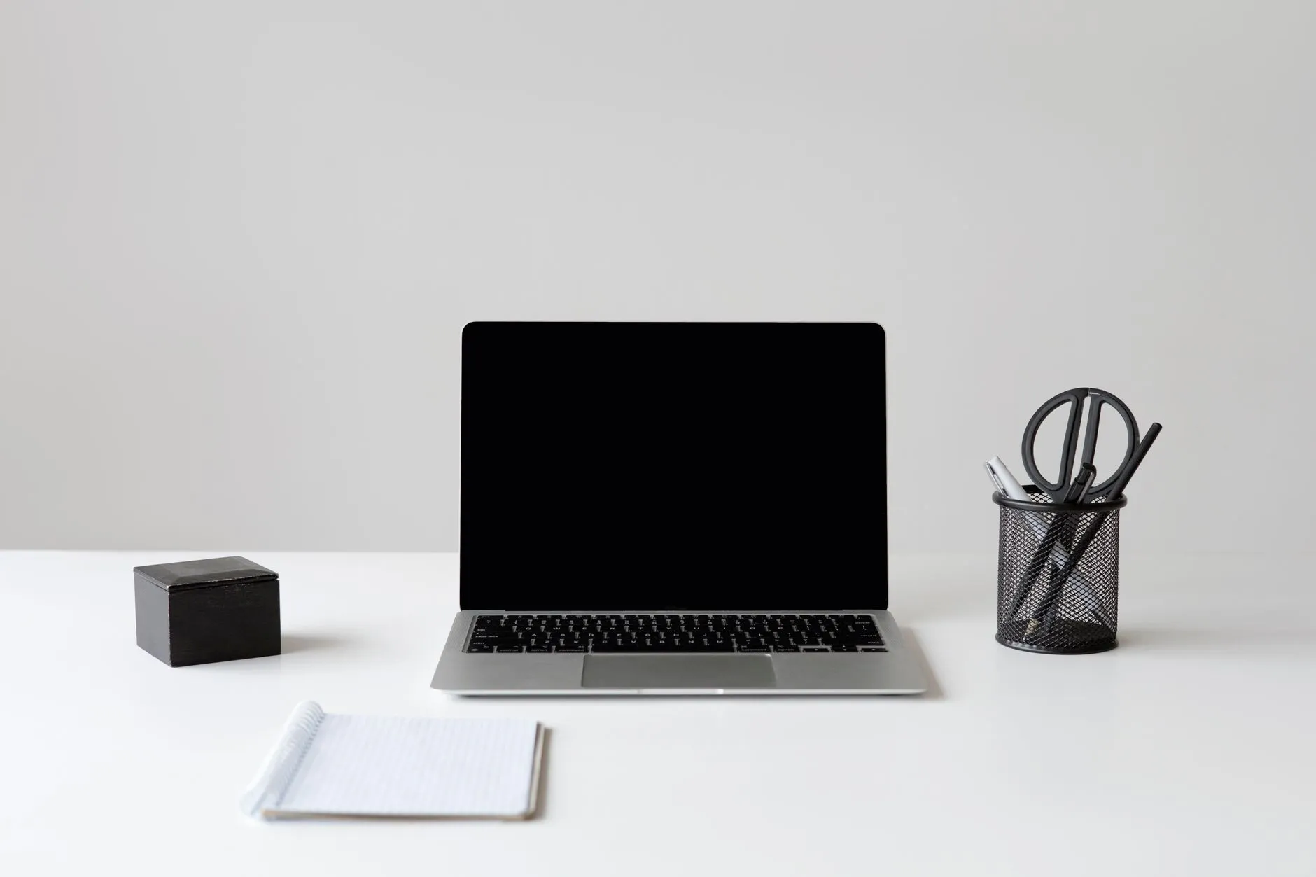 A laptop, notepad and pen holder on a clean white desk